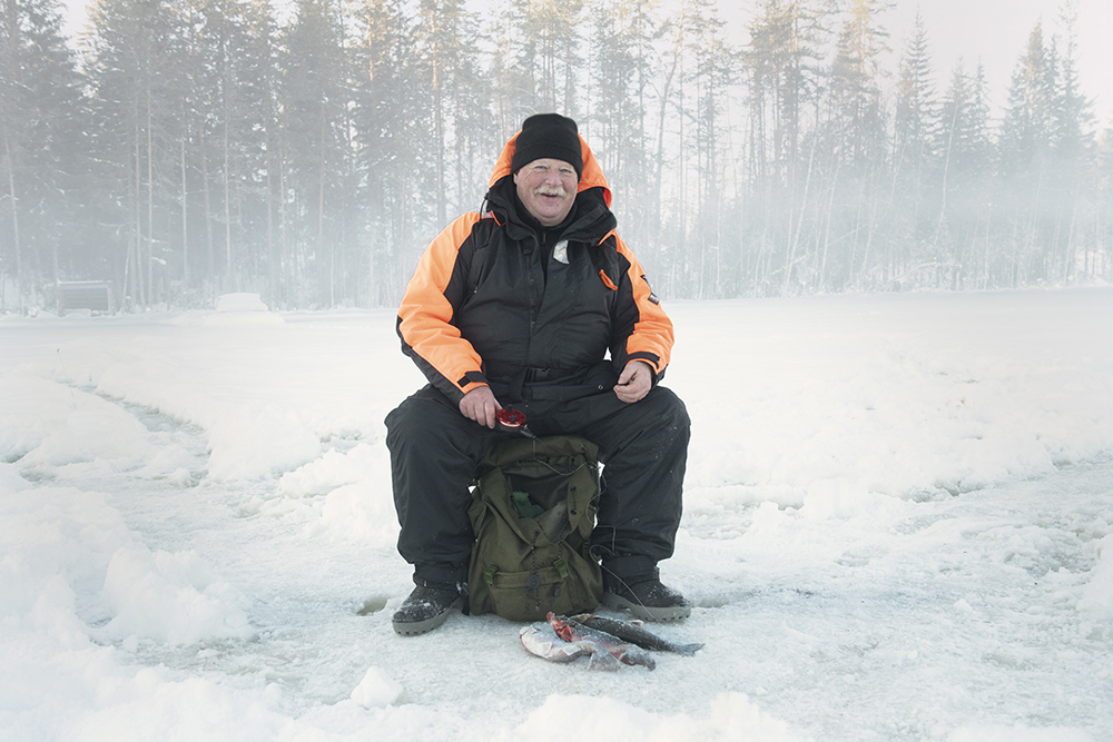 A happy man is sitting on a camping chair and winter fishing. In front of him lies several fishes.
