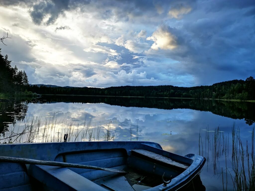 Blå kvällsbild. Roddbåten i förgrunden, moln på himlen som speglar sig i vattenytan. 